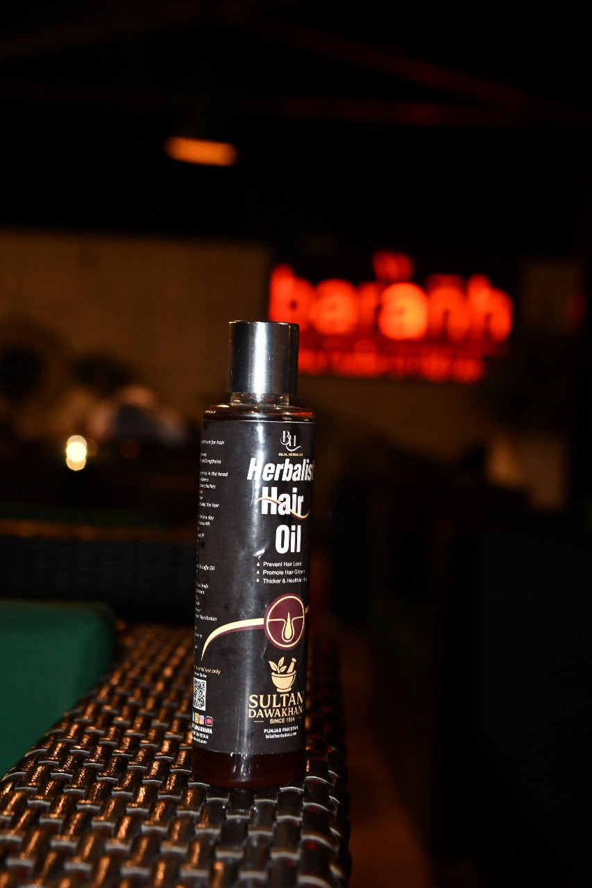 Bottle of Herbal Hair Oil on a dark surface with a blurred background
